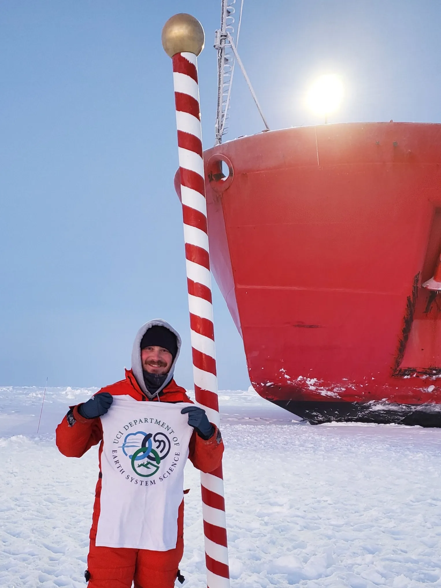 Researcher in polar gear standing on snow beside a research ship